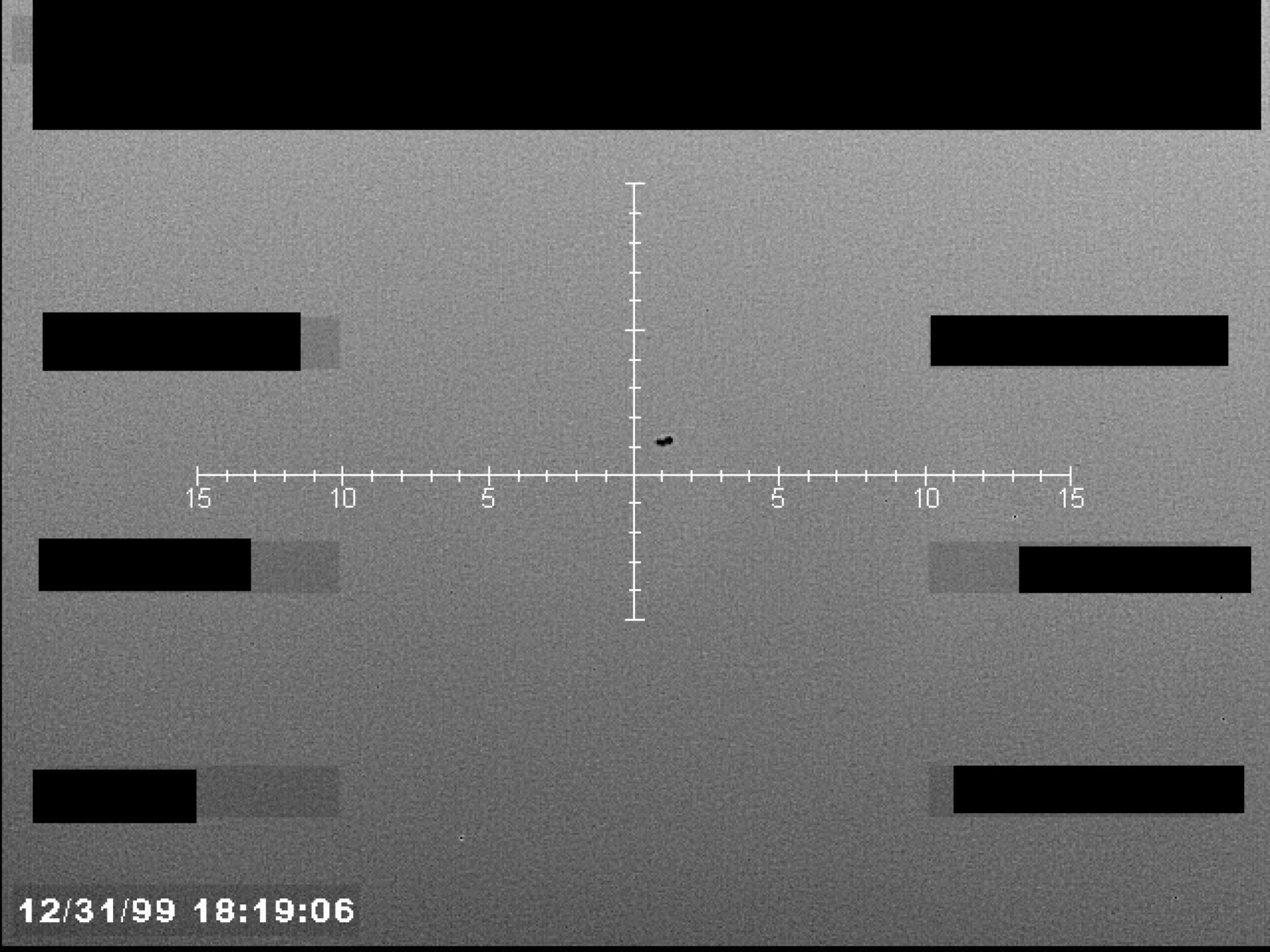 Sensor display with a central crosshair targeting a small, dark object. Numerical markings are visible along the horizontal axis of the crosshair. A timestamp is present in the lower-left corner.