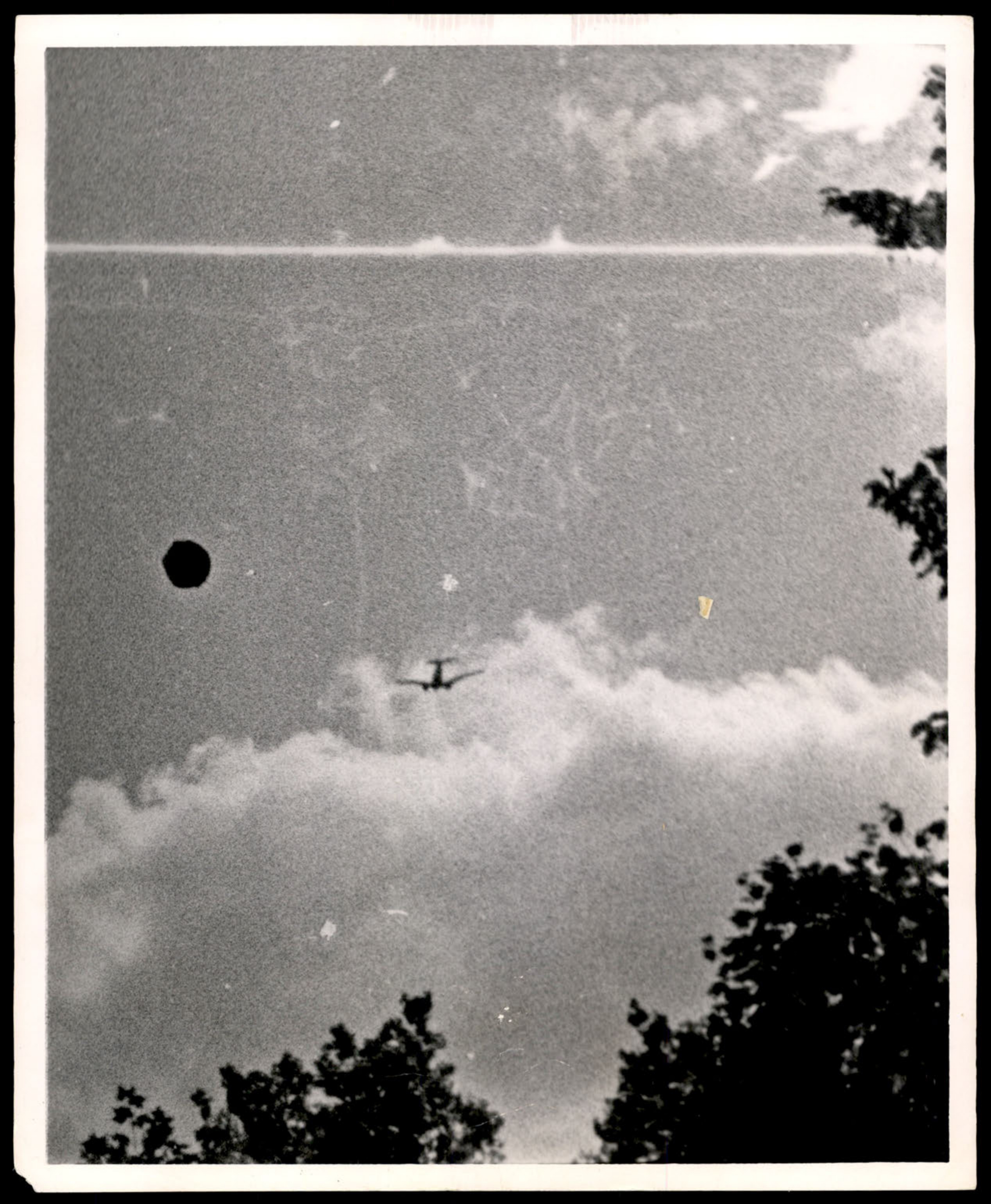 Photograph of a dark circular object and a conventional aircraft in a cloudy sky.